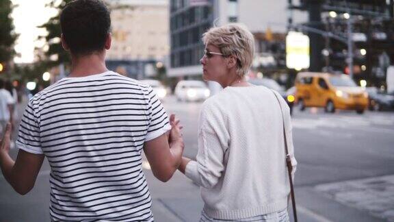 后景慢镜头快乐的年轻夫妇手牵着手走在纽约市美丽的街道享受约会之夜