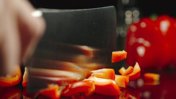 慢动作:厨师在黑色的桌子上切一个新鲜的红甜椒