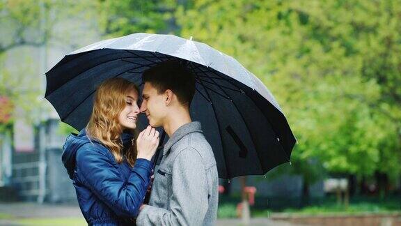 时尚的年轻夫妇在伞下拥抱下雨了