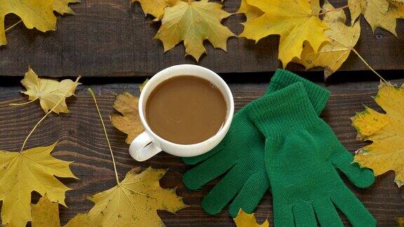 一杯咖啡一双绿色的手套旁边是枫叶放在木桌上