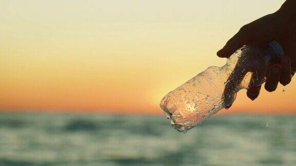 慢镜头的特写一个年轻的志愿者正在从海上捡起一个塑料瓶以保护夕阳下的环境