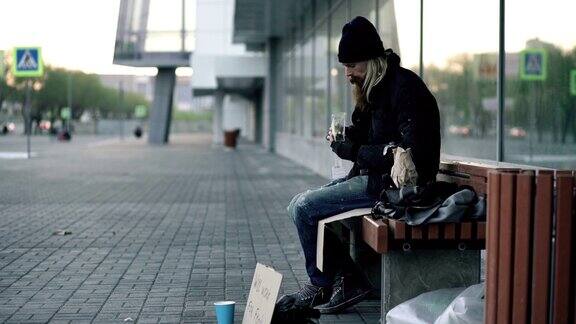 无家可归的年轻人晚上在城市街道的长椅上吃着三明治喝着纸袋里的酒