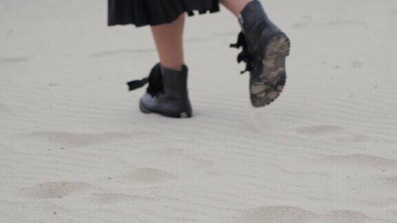 穿着靴子的女性腿和脚在寒冷的秋日沿着海边漫步女人踩在沙子上使用复制空间拍摄