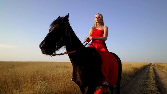 年轻的金发姑娘骑着马穿着红衣服在乡间小路上骑马