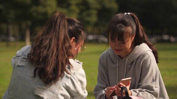 两个亚洲女大学生在校园里使用手机