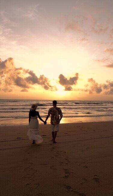 日落时分一对情侣走在泰国普吉岛的海滩上