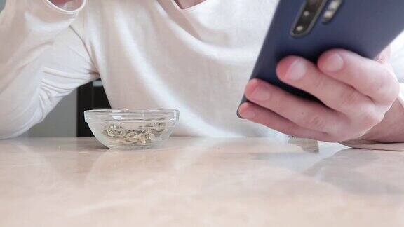 一名年轻人正在吃透明碗里的南瓜子手里拿着智能手机