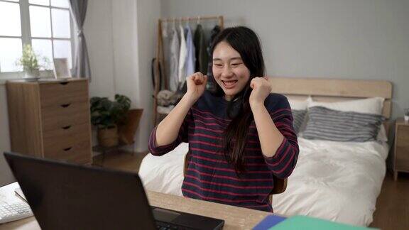 收到录取通知书电子邮件的韩国女生在家里握紧拳头欢呼并在电脑屏幕前查看细节