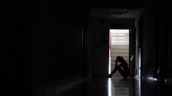 一个悲伤的年轻女孩的剪影坐在黑暗中