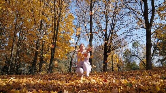 一个女人把秋天落下的五彩缤纷的枫叶高高兴兴地扔了起来