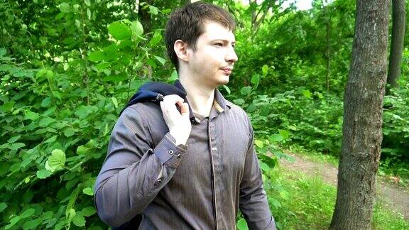 一个年轻人站在树林里把夹克扔到肩上慢动作