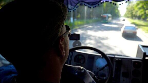 在阳光明媚的日子里在城市道路上行驶的货车司机在车厢里享受旅程戴着帽子和太阳镜的男人控制着他的卡车专注地看着道路内景慢镜头