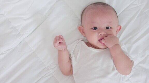可爱的亚洲新生婴儿的肖像躺在白色的床上玩看着相机笑着笑着开心的脸天真可爱的小婴儿