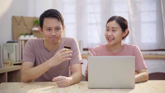 年轻的亚洲夫妇使用笔记本电脑和信用卡在家里网上购物