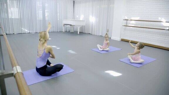 在芭蕾课上教练和两个女孩坐在垫子上做芭蕾表演