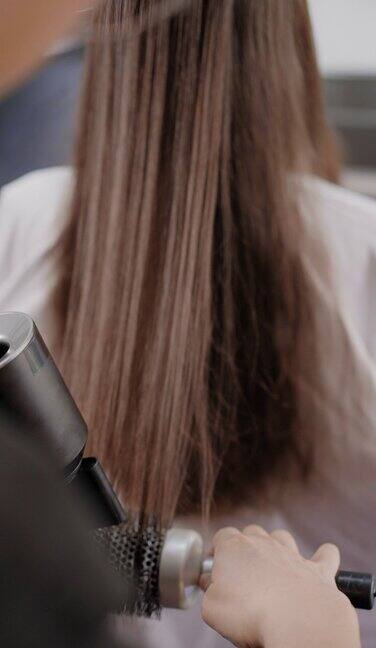 美发师的后视镜是在美发沙龙用电吹风吹干女客户的长发使头发变直