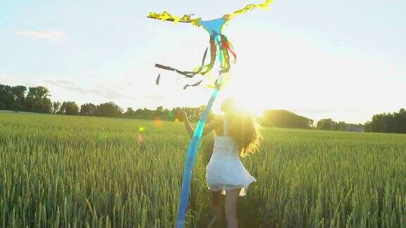 美丽的女孩带着风筝在风中飞翔在日落的麦田里奔跑