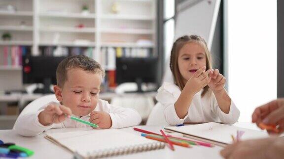 可爱的女孩和男孩在笔记本上画画坐在桌子上幼儿园