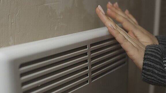 一个俄罗斯女人正在一个寒冷的房子散热器取暖自己与供暖的问题加热房间与一个电对流