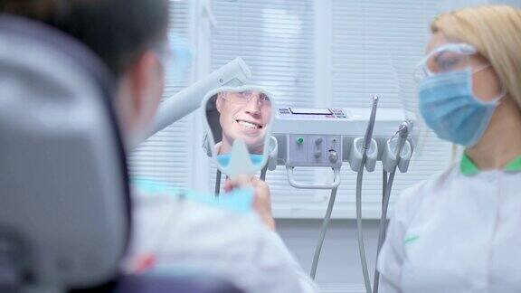 男人看着牙医的镜子欣赏他的微笑漂亮整齐的牙齿满意的病人看着牙医的镜子这是牙科治疗的结束