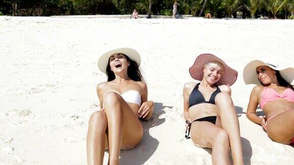 三个女孩躺在沙滩上的比基尼和草帽享受日光浴谈话快乐的女人游客在暑假