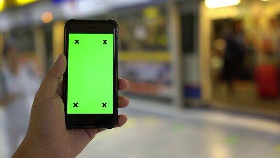 手持智能手机的近距离看绿色屏幕色度键显示在火车站使用手机通过滚动、滑动、手指来触摸屏幕