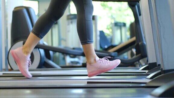 近距离的女人的腿在健身房做有氧运动训练跑步机上穿着粉红色的运动鞋