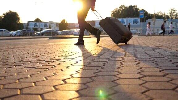 一个成功商人带着行李从机场走在城市的街道上日落时分年轻经理的双腿去停车场拖着带轮子的行李箱慢镜头