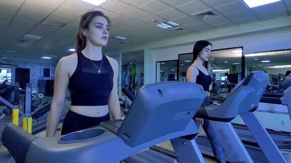 在健身房两个漂亮的女孩在跑步机上散步慢动作