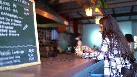 一名年轻女子在酒吧柜台使用智能手机