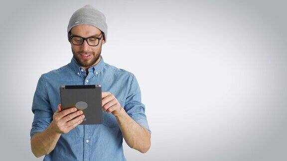 中景的一个时尚的年轻人在帽子和眼镜持有和使用平板电脑拍摄在一个白色的背景