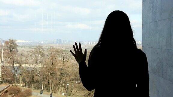 沮丧的年轻女子透过大窗户望着美丽的公园