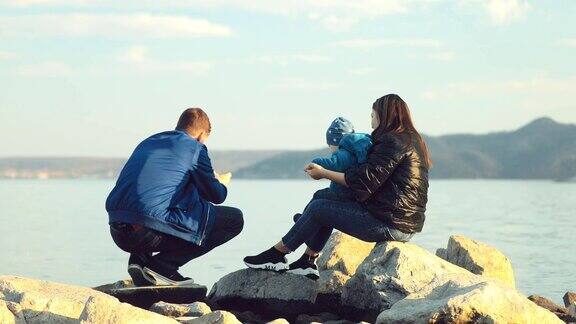 丈夫和妻子坐在海滩上的大石头上把石头扔进水里家人在海边从后面看相机