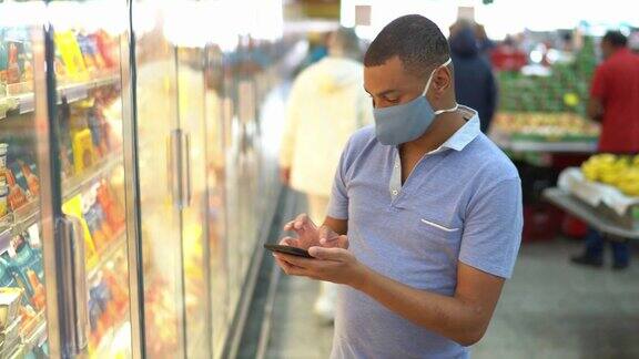 一名男子戴着口罩在超市买东西时使用智能手机