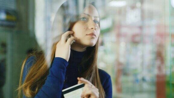 一个迷人的女人正在讲电话透过商店的玻璃柜往外看购物选择和购物概念