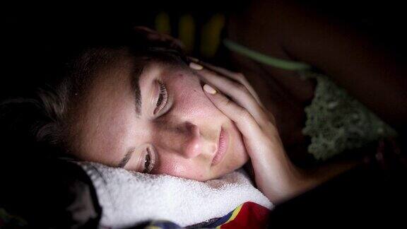疲惫的年轻女子躺在一边看智能手机试图获得一些睡眠