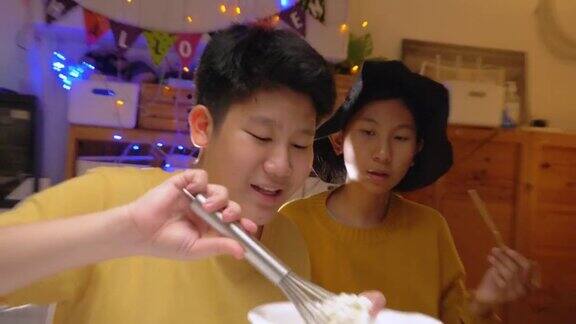亚洲女孩戴着女巫的帽子晚上和哥哥一起在家做糖霜饼干万圣节的生活理念