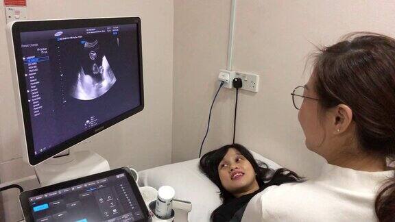 亚洲华人年轻医生正在医院医务室为孕妇做超声波检查