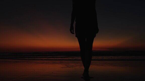 一个穿着短裤的年轻女子在日落时分在海边散步的黑色剪影美丽快乐的女游客在海边的夜空背景