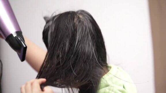 一位中年亚洲妇女在家里用吹风机吹头发