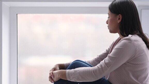 一个孤独的非洲女人坐在窗台上透过窗户向外看