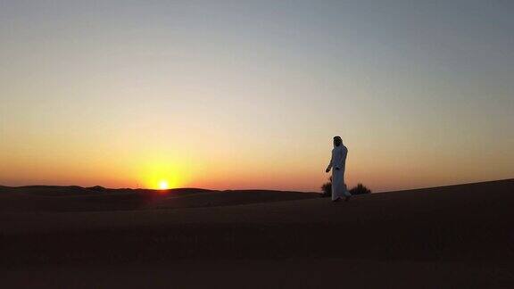 一个阿拉伯人在日落时漫步在沙丘上