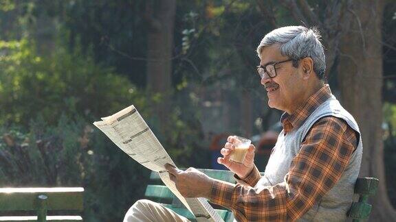 老人在公园长椅上喝茶看报纸