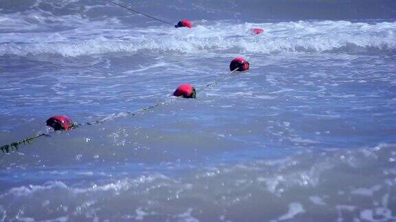 用绿色海藻围起来的红色旧浮标漂浮在海上的波浪上