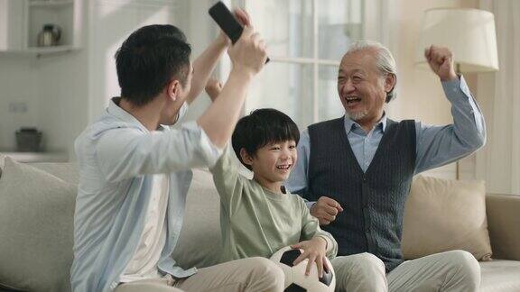 亚洲儿子父亲和祖父正在电视上观看足球比赛的直播