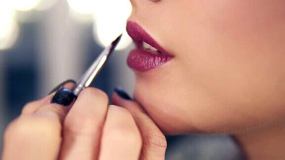 不可辨认的专业化妆师用特殊的刷子在模特的嘴唇上涂口红