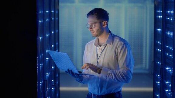 男网络工程师站在服务器室用笔记本电脑检查系统在数据中心人员服务器专家检查工作系统和机架服务器计算机机柜的硬件