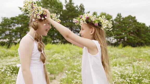 夏日里两个女孩戴着花圈在盛开的草地上玩耍快乐的少女在乡村夏天的田野上玩花圈
