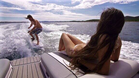 一个年轻人在船后冲浪一个女人在晒日光浴