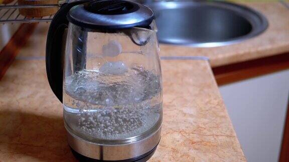 泡沫在水沸腾的玻璃电水壶在背景厨房